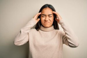 Young beautiful asian woman wearing casual turtleneck sweater over white background suffering from headache desperate and stressed because pain and migraine. Hands on head.