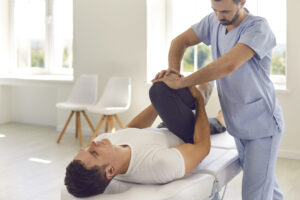 Chiropractor helping male athlete do physical exercise during rehabilitation