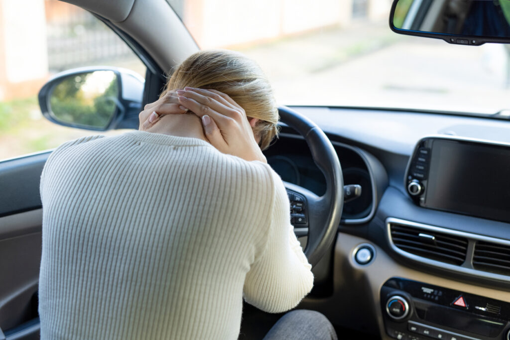 Woman suffering from neck pain in the car feeling stressed out and alone.